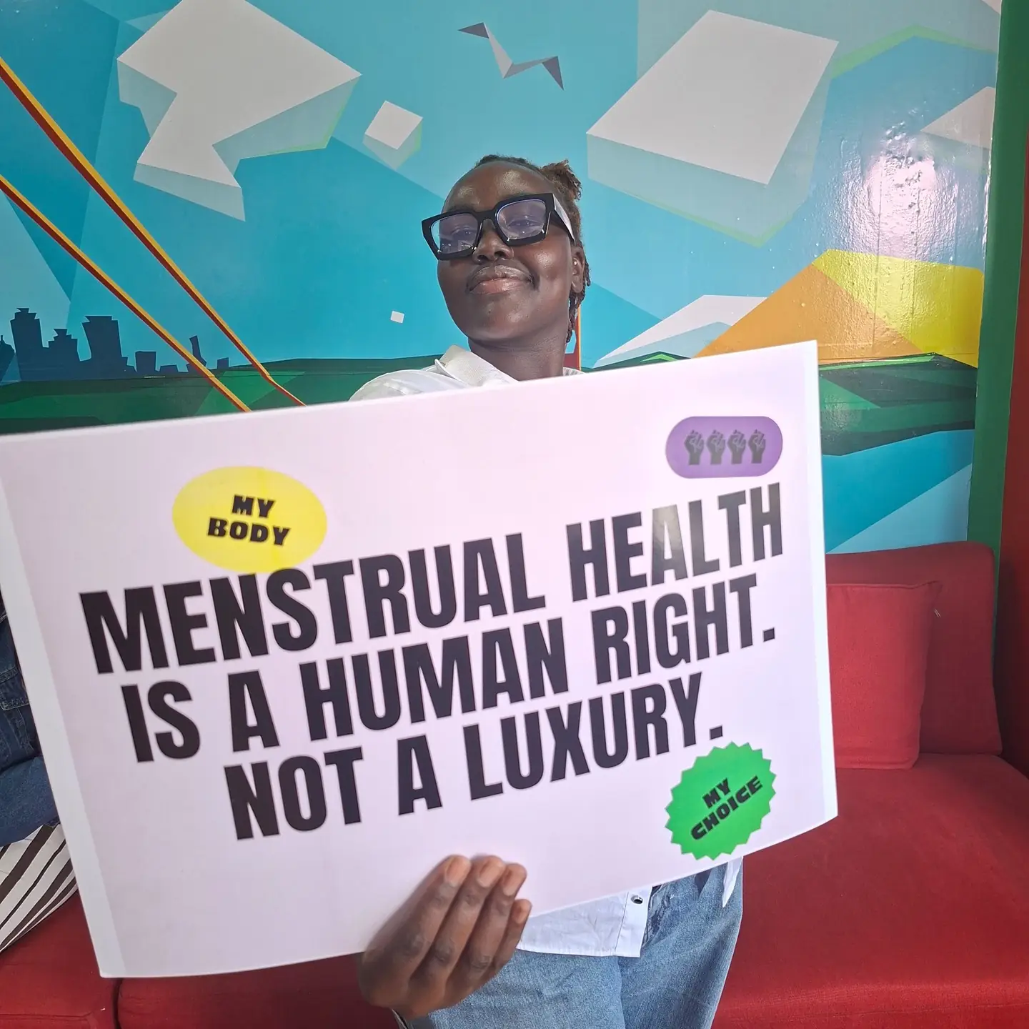 A smiling participant holds a large Menstrual Health Is a Human Right, Not a Luxury placard.
