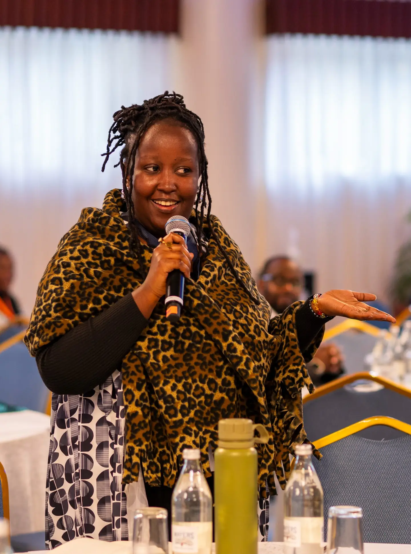 A Wazi participant smiles and gestures while speaking into a microphone at the symposium.