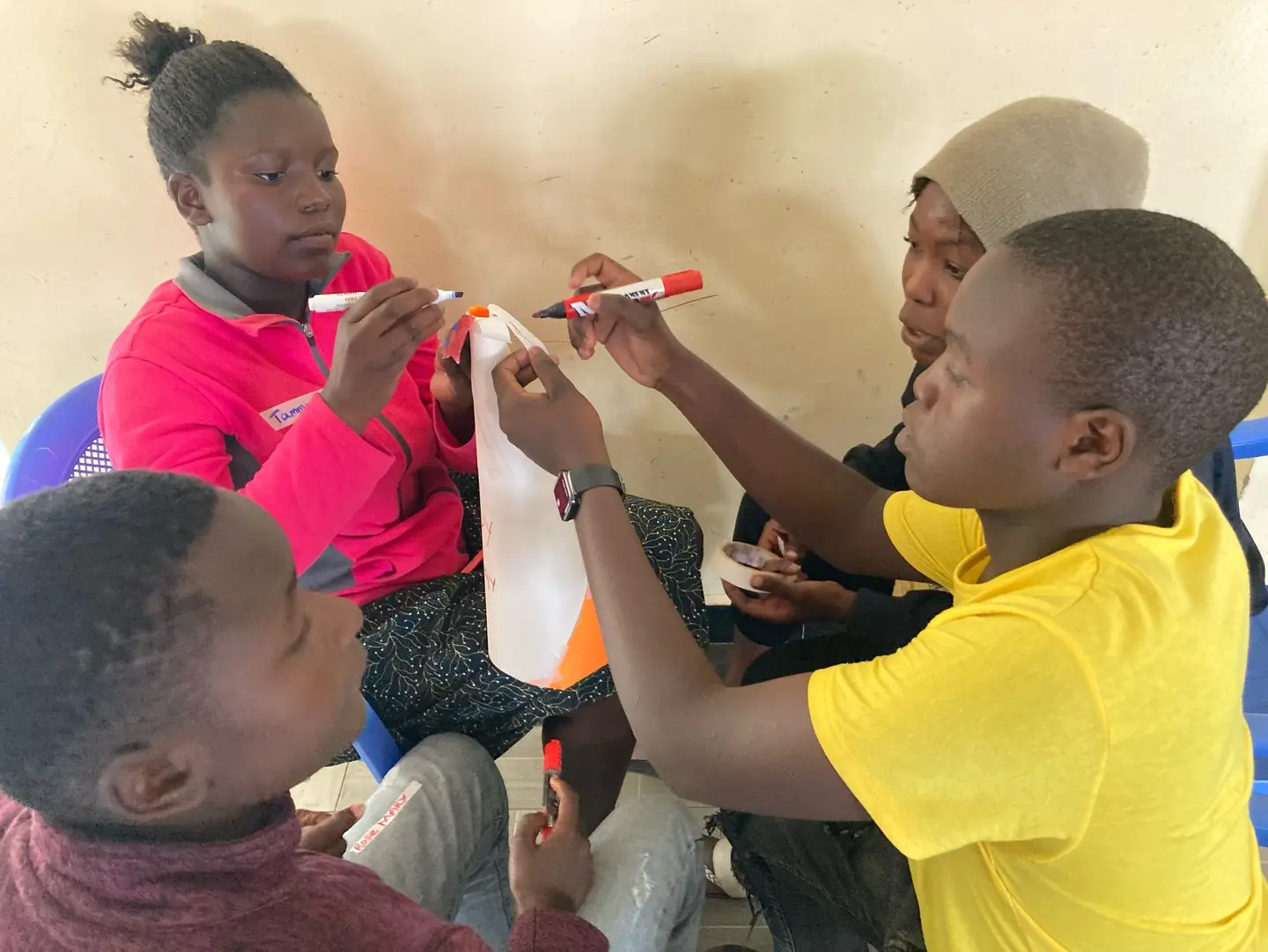 Teenagers collaborate over coloured paper while making thinking hats in a classroom.
