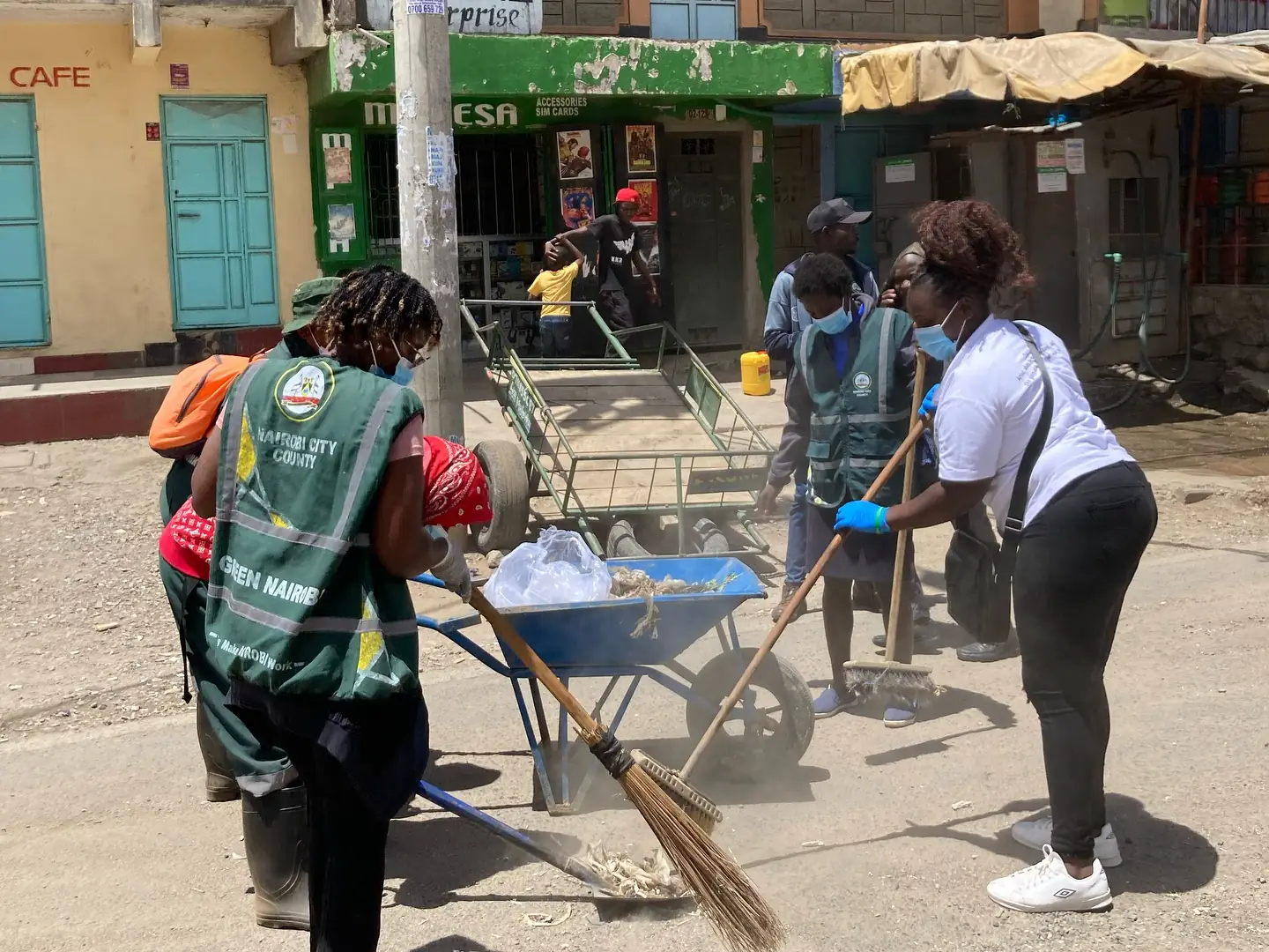 Volunteers sweep a neighbourhood street and collect waste in a wheelbarrow.