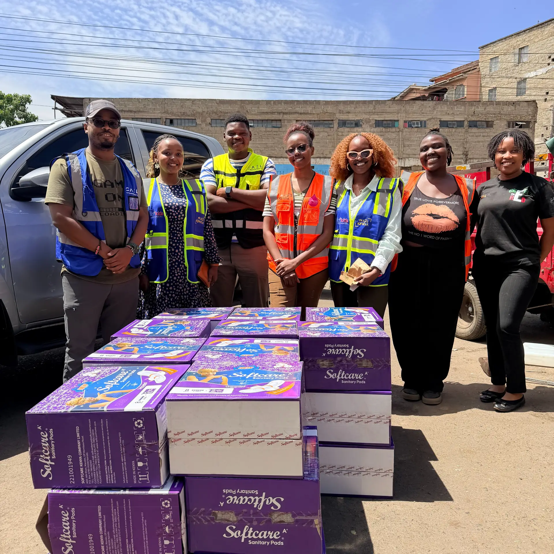 Wazi and CAEL volunteers stand beside cartons of sanitary pads for schools.