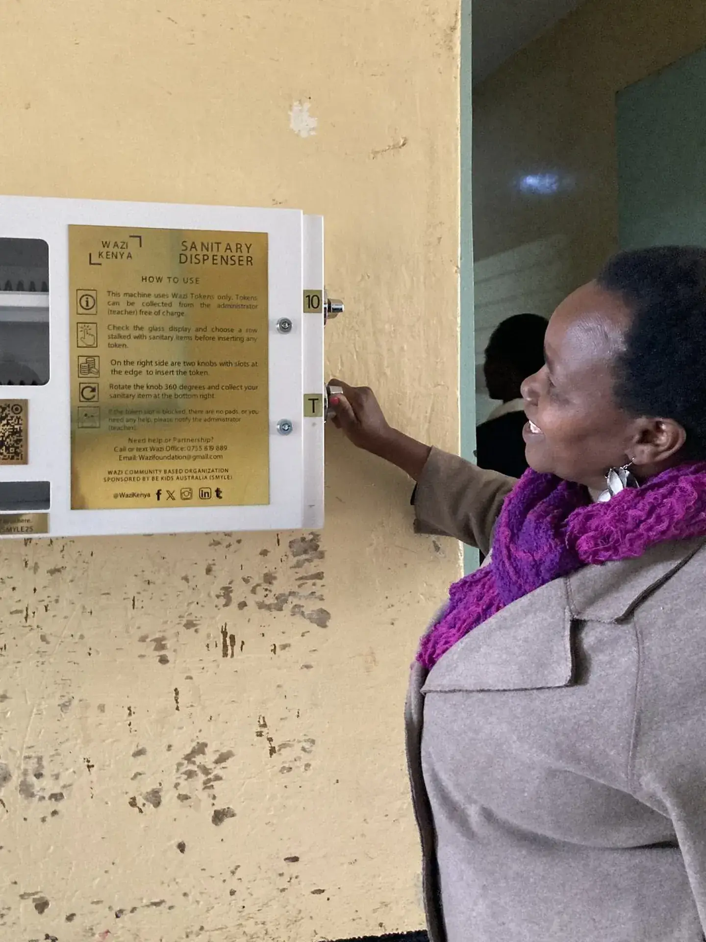 A woman turns the handle of a wall-mounted Wazi sanitary dispenser.